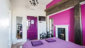 Un dormitorio con una cama grande, un aparador, un espejo, una chimenea y una puerta que da a otra habitación.