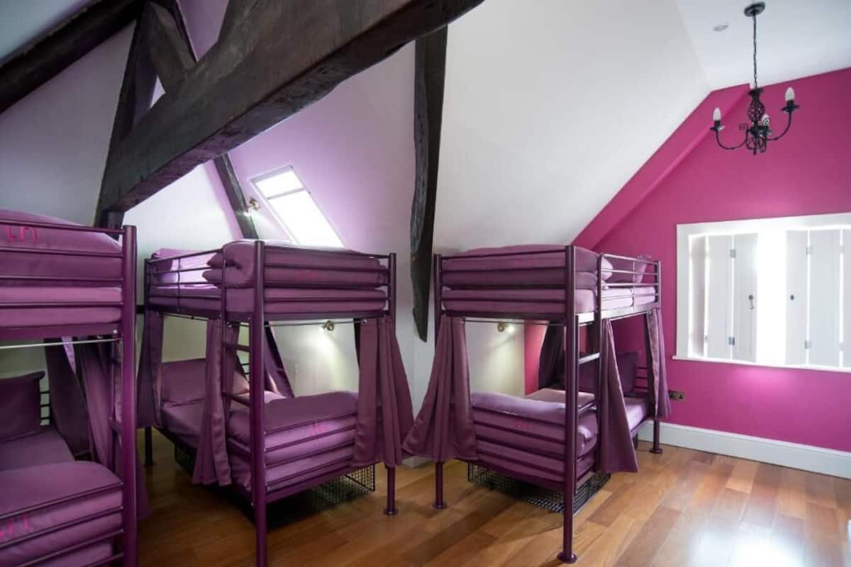 A room with bunk beds, wooden beams, a window, and a chandelier.