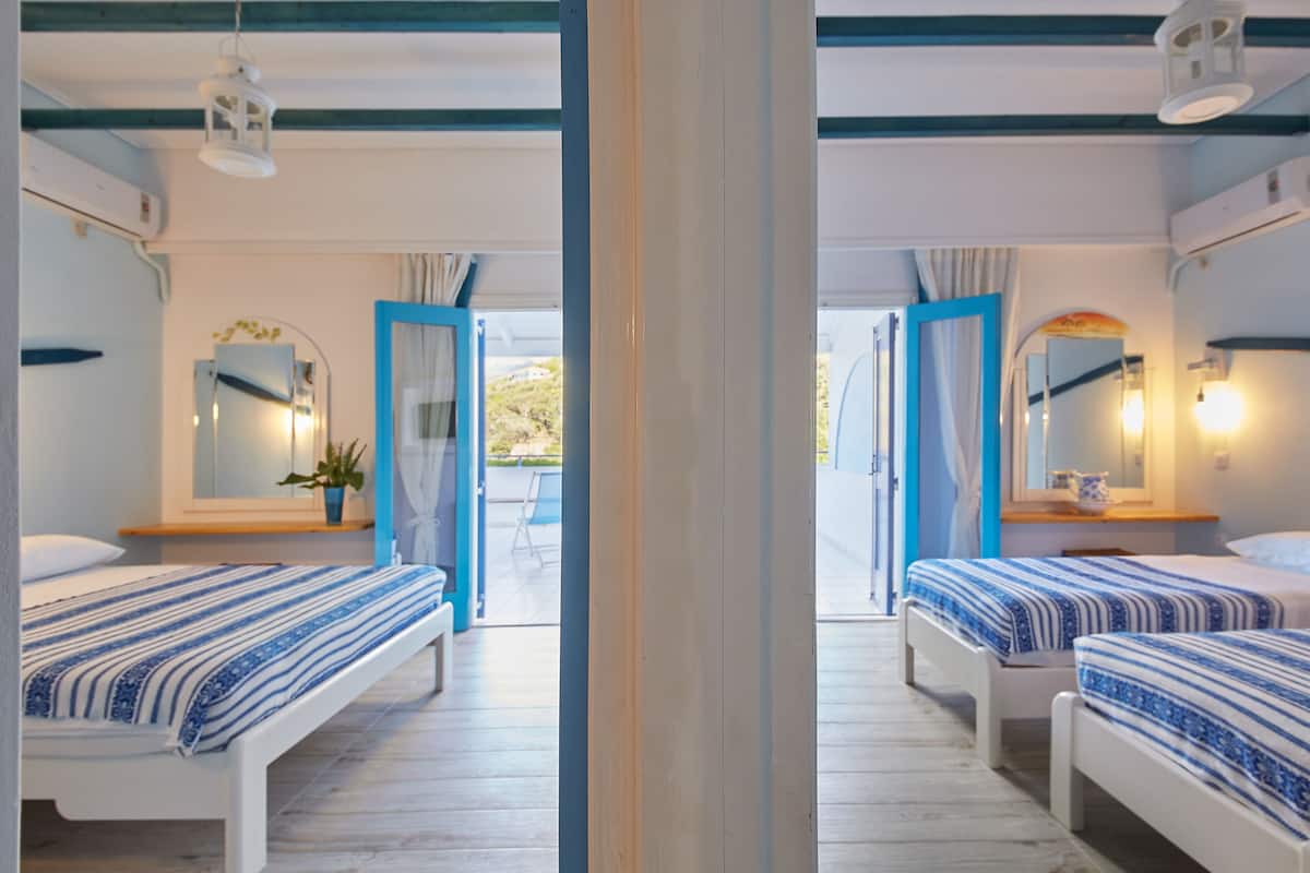A hotel room with two beds, a wooden floor, a mirror, a window with curtains, and a door leading outside.