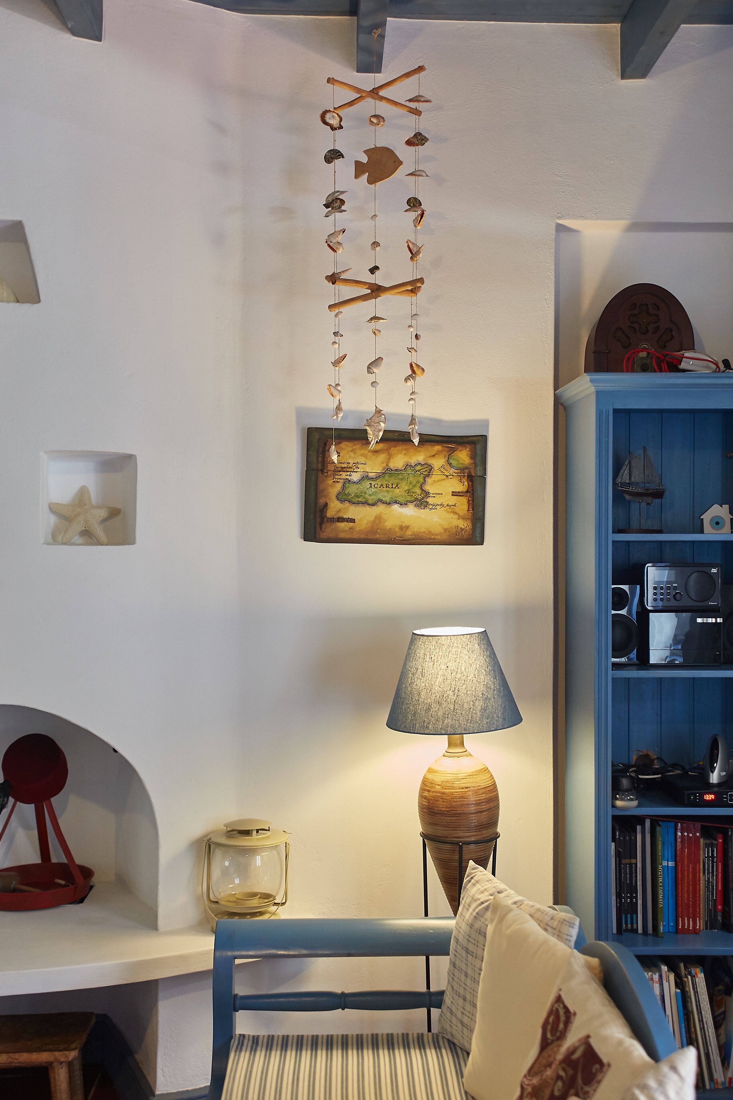 A cozy living room with a blue armchair, a lamp, a map, and a bookshelf.