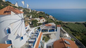 A coastal village with white buildings, a windmill, and a view of the sea. - Kerame Studios (Ikaria)