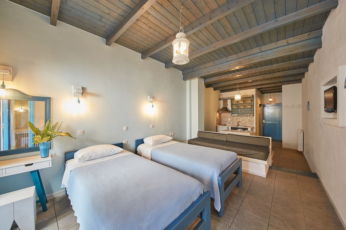 A bedroom with two beds, a desk, a mirror, and a hanging light fixture.