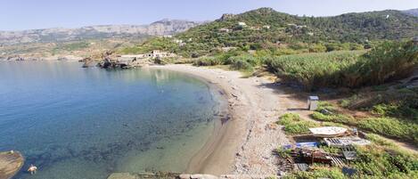 Un paisaje costero con una playa despejada, costa rocosa y edificios dispersos en una ladera.