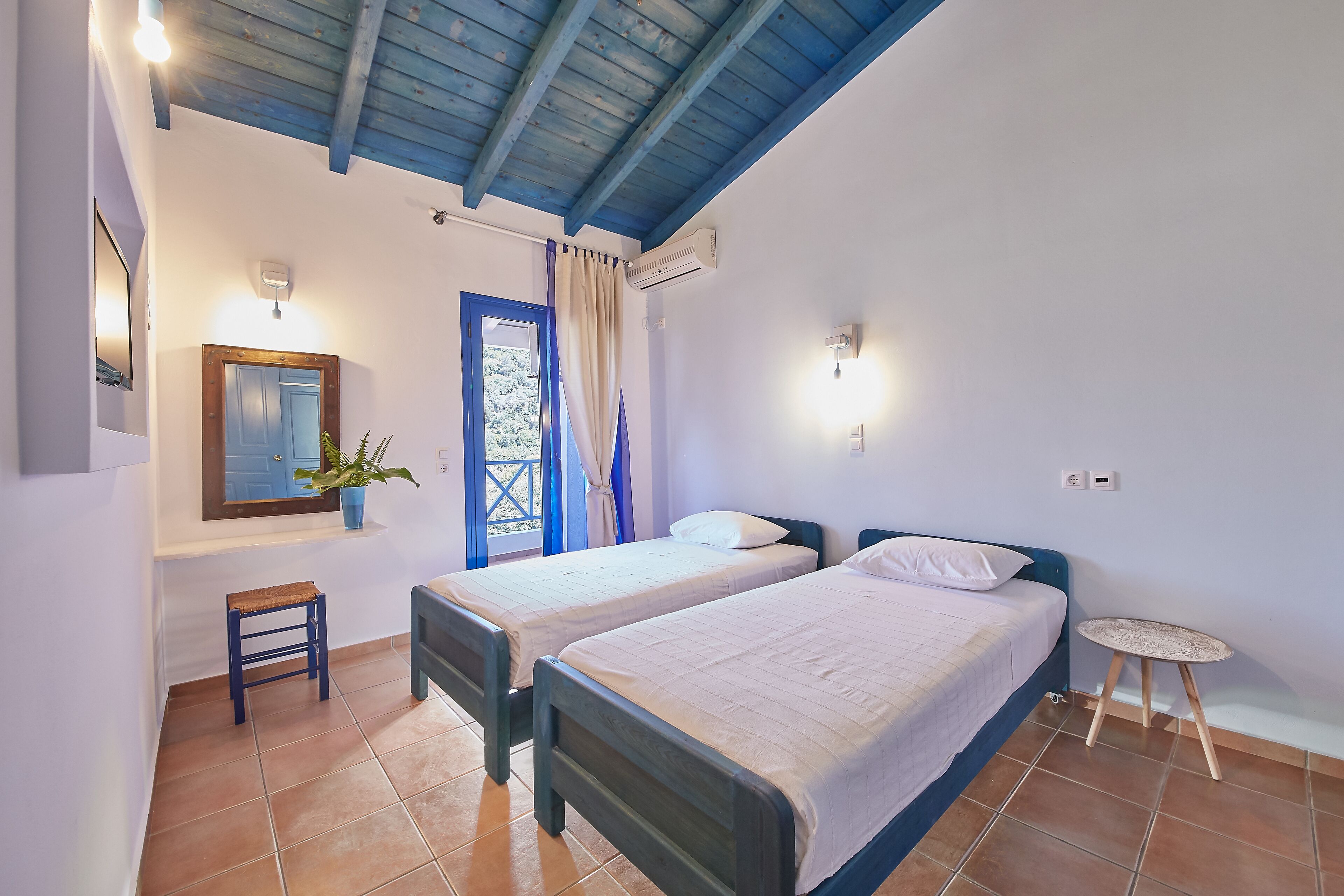 A bedroom with two single beds, a small stool, a potted plant, and a window with curtains.