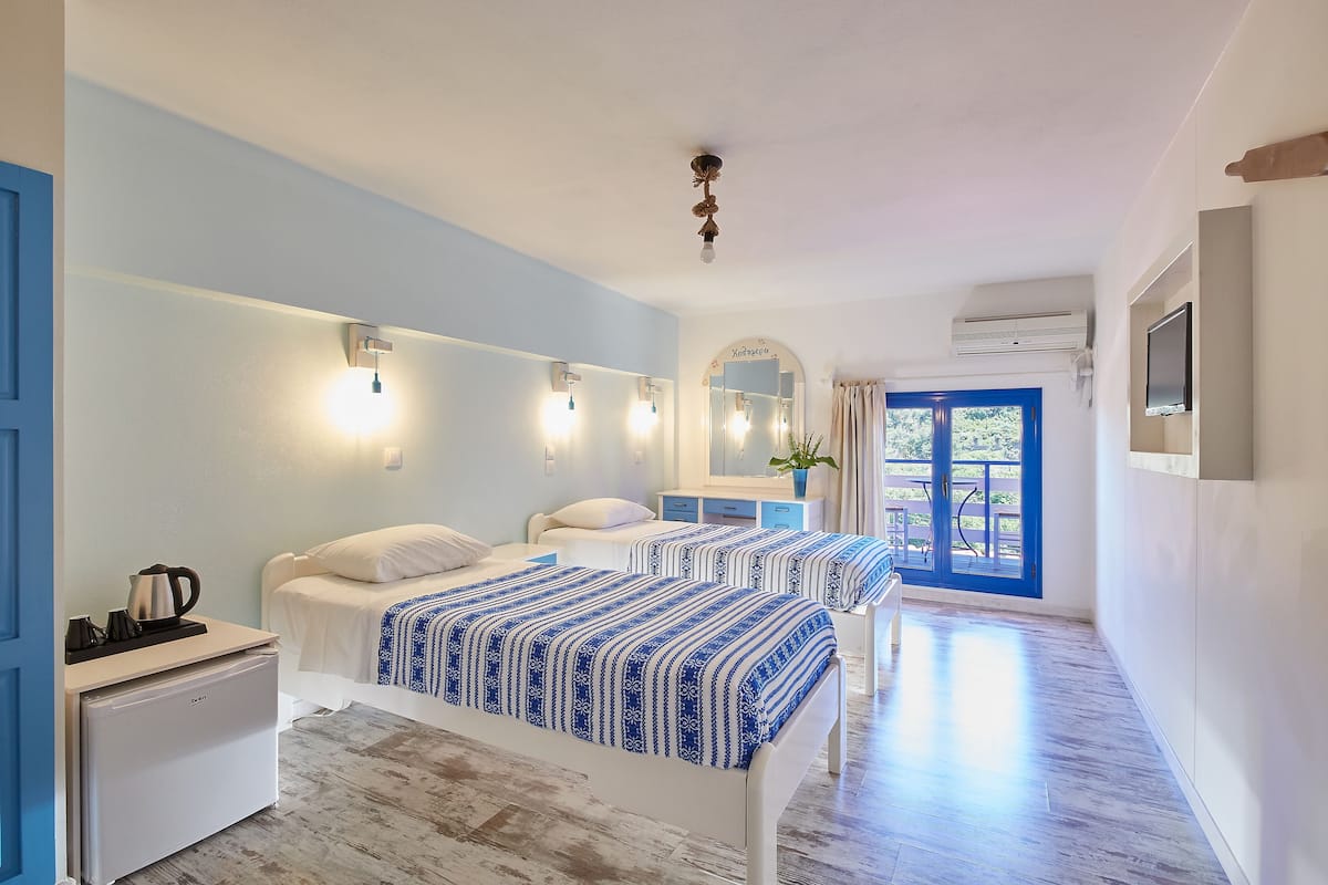 A hotel room with two beds, a small kitchenette, a bathroom with a mirror, and a view of the outdoors.