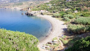 A coastal landscape with a sandy beach, rocky outcrops, and scattered buildings. - Kerame Studios (Ikaria)