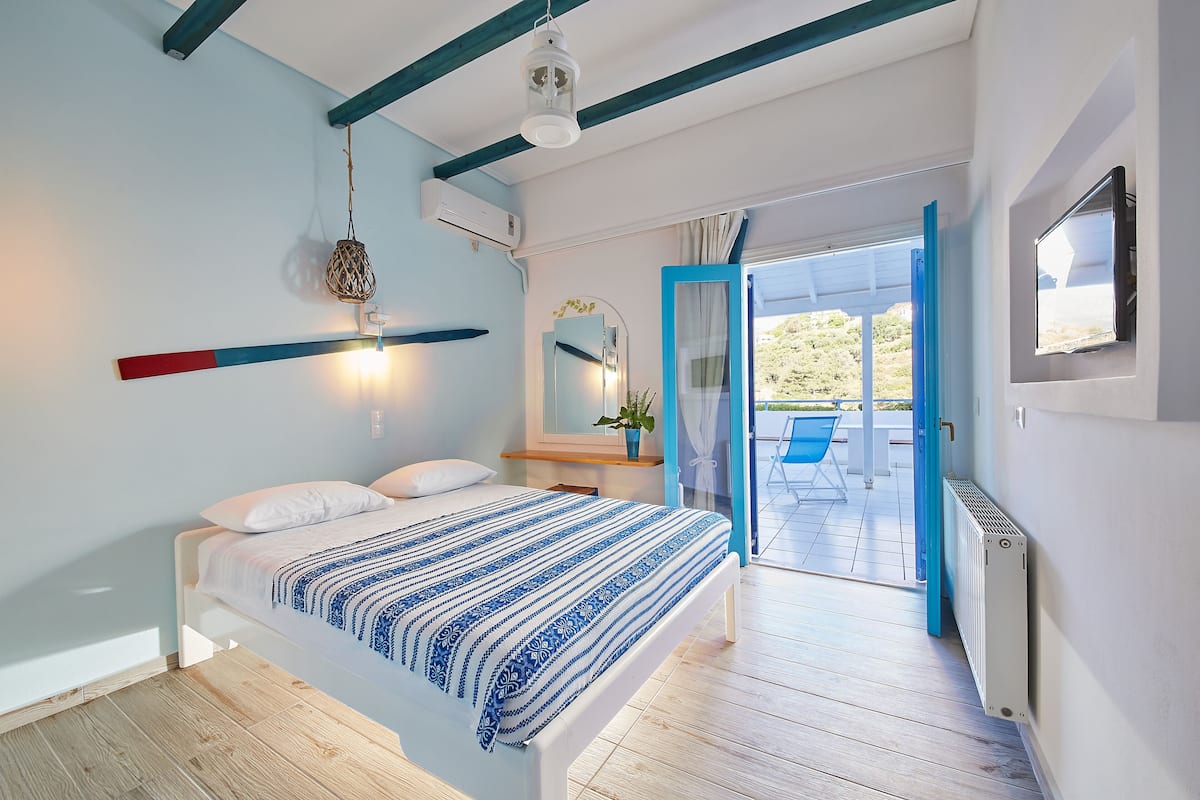 A modern bedroom with a bed, a hanging light fixture, a mirror, and a view of an outdoor area.