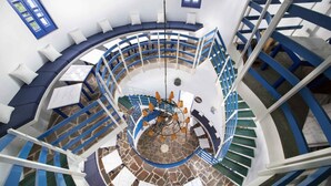 A spiral staircase with blue railings and white steps, leading to a seating area with blue cushions and a chandelier. - Kerame Studios (Ikaria)