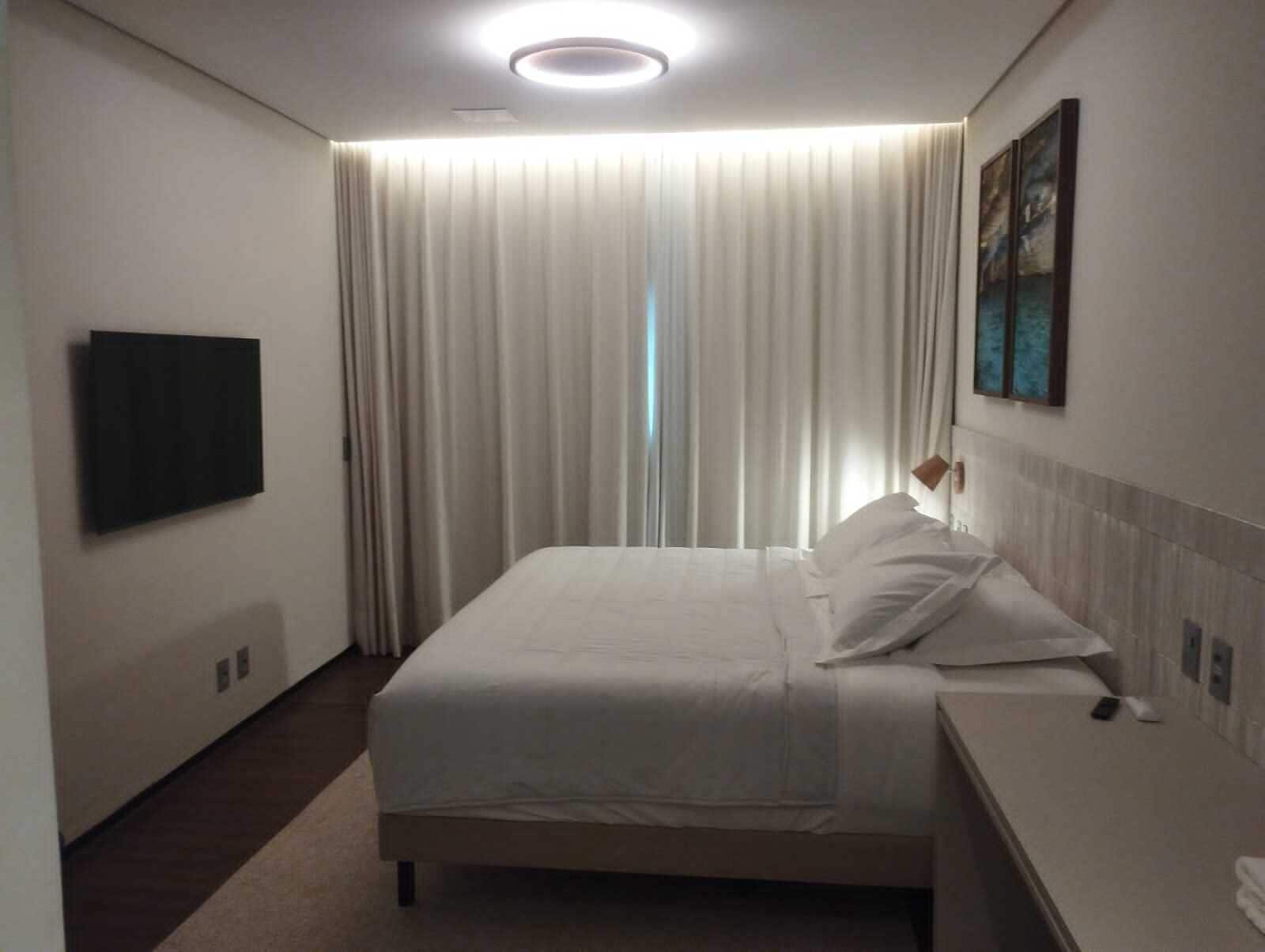 A hotel room with a bed, a flat-screen TV mounted on the wall, and a painting on the wall.