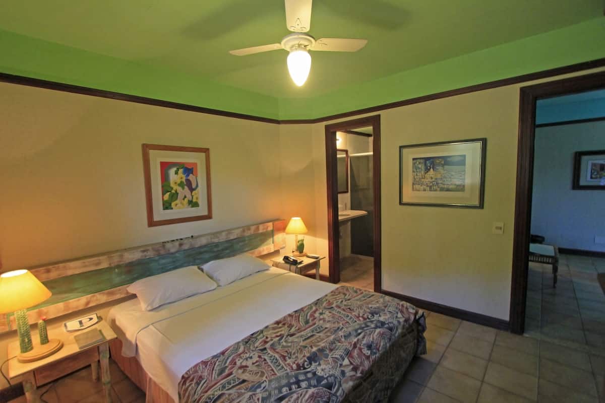 Habitación de hotel con cama, dos lámparas de noche, ventilador de techo y cuadros en las paredes.