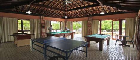 A pool hall with two pool tables, a billiards table, and a ceiling fan.