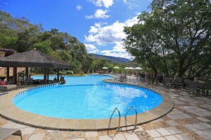 A swimming pool with a tiled deck, lounge chairs, umbrellas, and a thatched-roof pavilion. - Hotel Portal Lençóis (Lençóis)