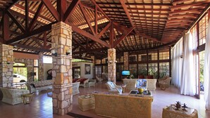 A spacious lobby with stone pillars, wicker furniture, and a large TV screen.