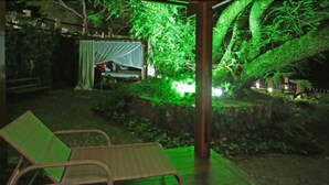 A covered outdoor area with a table and chairs, surrounded by lush greenery and a small waterfall.