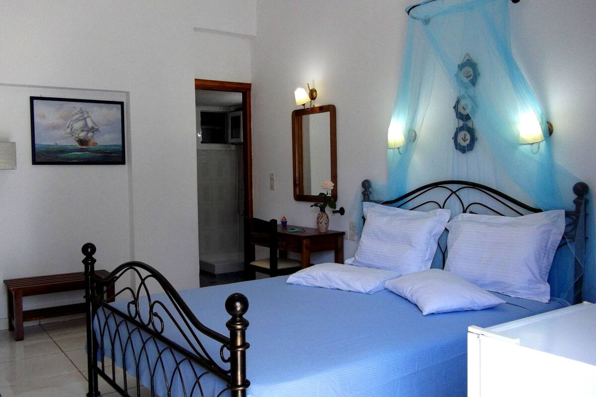 A bedroom with a bed, a bedside table, a mirror, a window with curtains, and a painting on the wall.