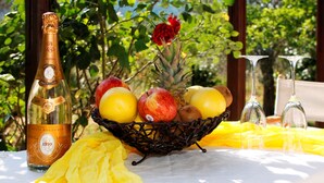 Una botella de champán, una cesta de frutas y dos copas sobre una mesa con un mantel amarillo.