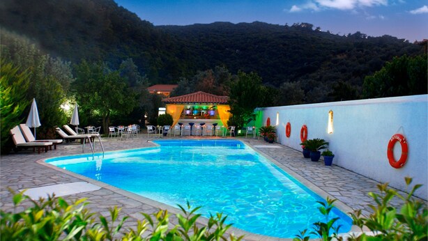 Una piscina con sillas de descanso y sombrillas, con montañas al fondo.