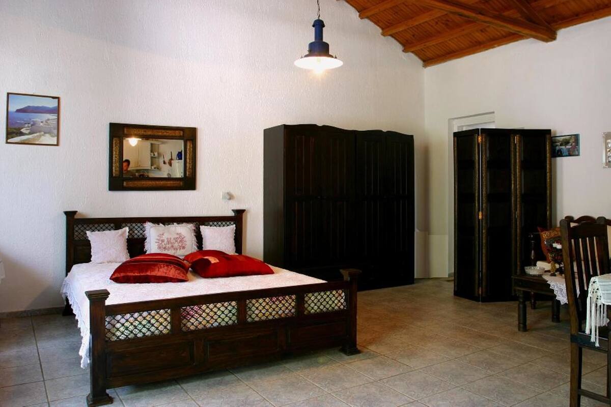 A bedroom with a wooden bed, a wardrobe, a mirror, and a hanging light fixture.