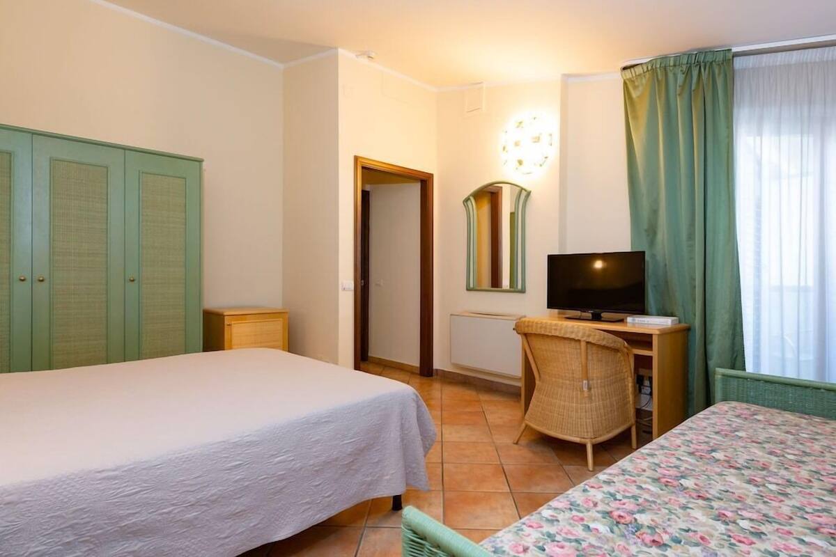 A hotel room with a bed, a desk with a television, a chair, and a wardrobe.
