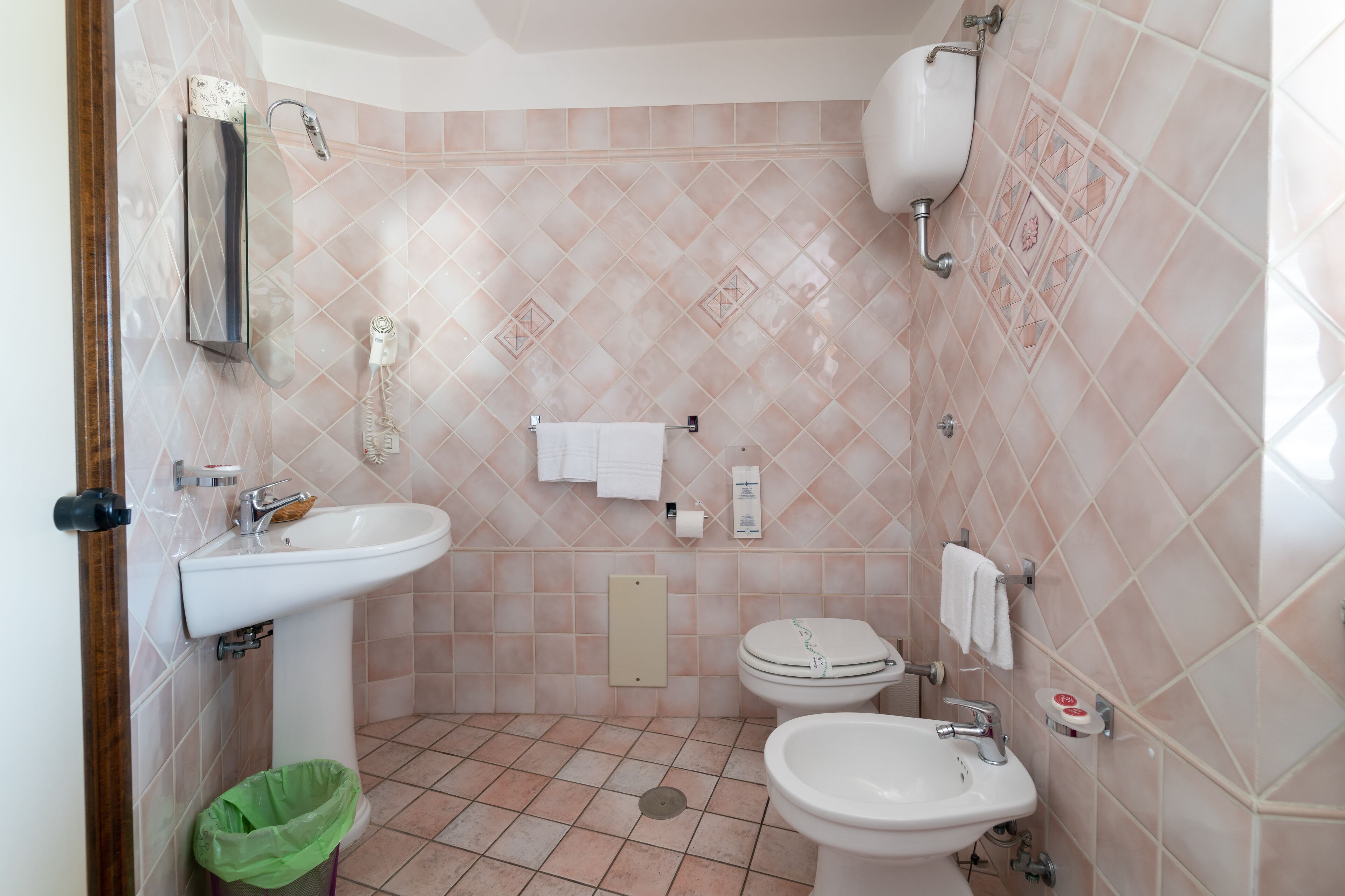 A bathroom with a sink, toilet, and bidet, tiled in a diamond pattern.