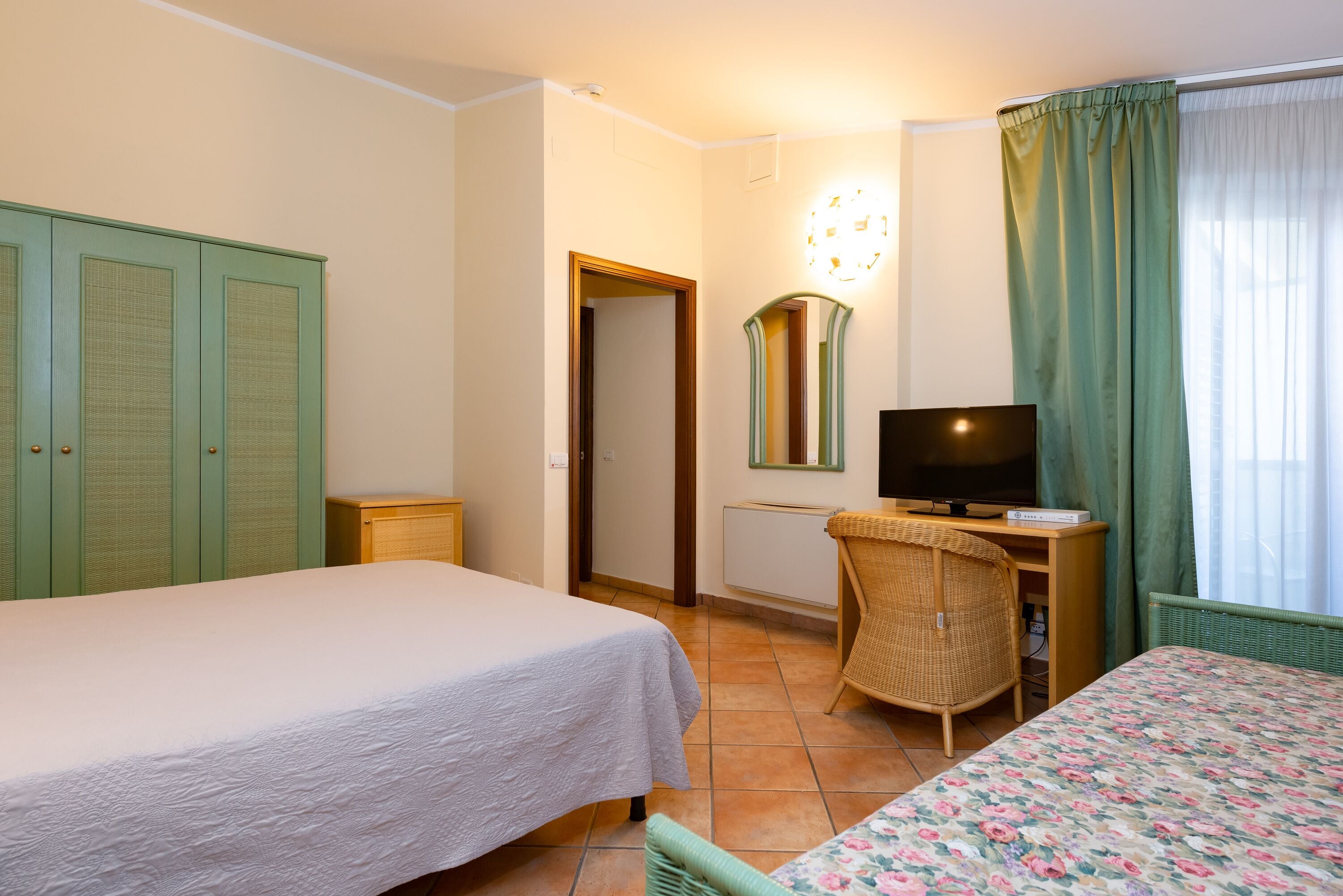 A hotel room with two beds, a television, a desk, and a wicker chair.