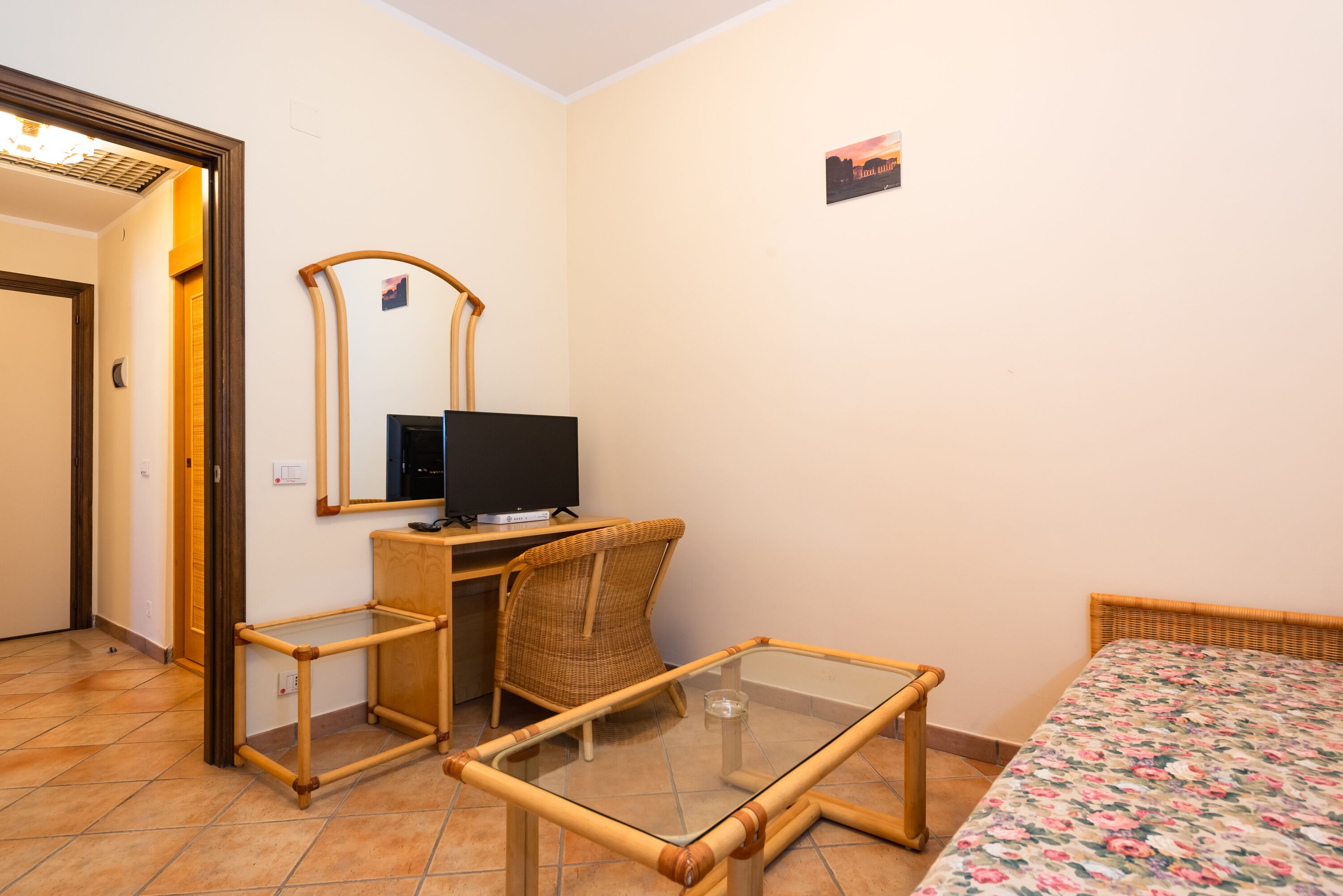 Una stanza con un letto, un tavolino, una sedia, una televisione e uno specchio.