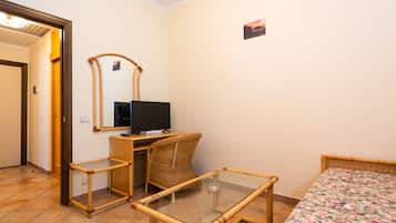 A room with a bed, a small table, a chair, a television, and a mirror.