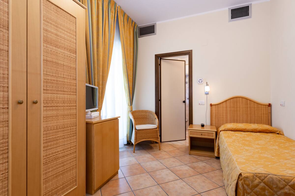 A hotel room with a bed, a chair, a desk with a computer, and a wardrobe.