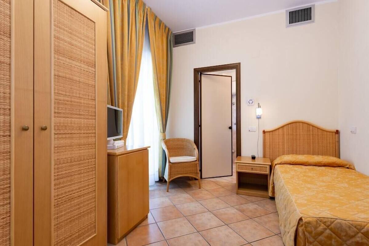 A hotel room with a bed, a desk with a chair, a wardrobe, and a television.