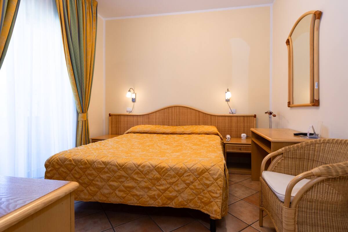 A hotel room with a bed, bedside tables, a chair, and a mirror.