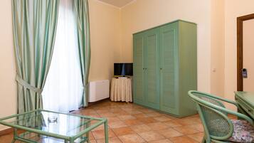 Ein Zimmer mit Glastisch, grünem Sessel, Kleiderschrank und Fernseher auf einem kleinen Tisch.