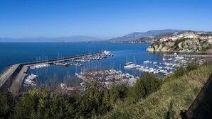 A marina with boats docked, a pier extending into the water, and a town on a hillside in the background.