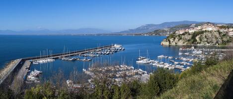 Un puerto deportivo con barcos amarrados, un muelle que se adentra en el agua y un pueblo en la ladera al fondo.