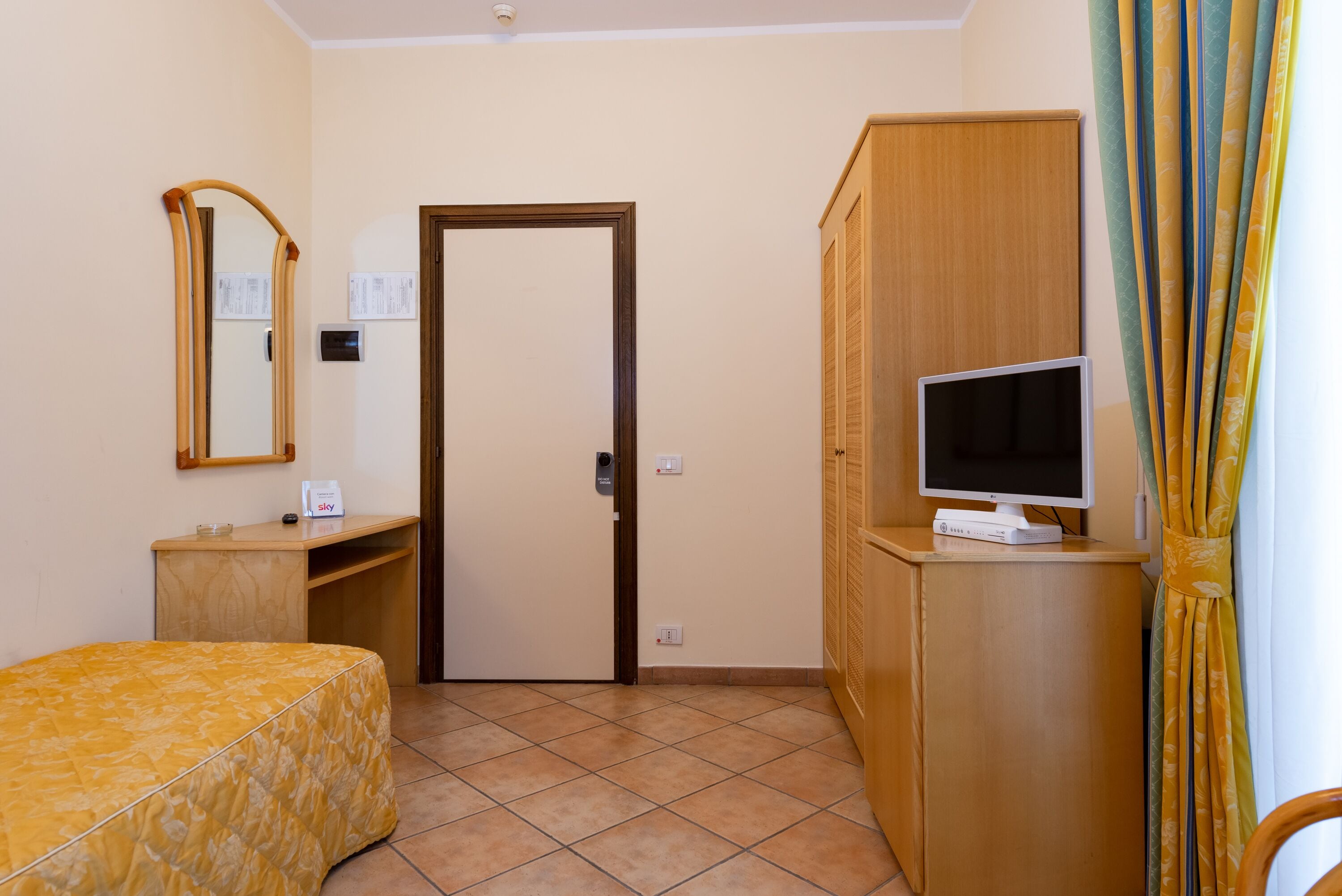 A hotel room with a bed, a desk with a computer, a television, and a wardrobe.