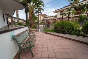 A patio area with a bench, a tiled floor, and a view of a residential building with balconies and plants.