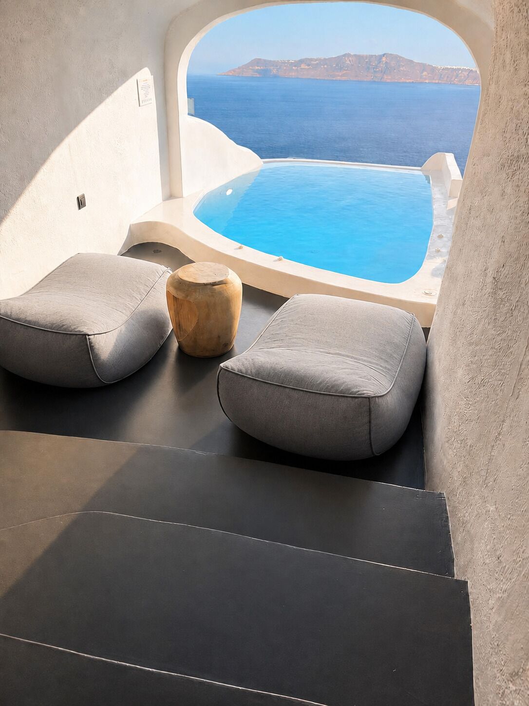 A modern bathroom with a bathtub, two grey cushioned seats, and a wooden stool.