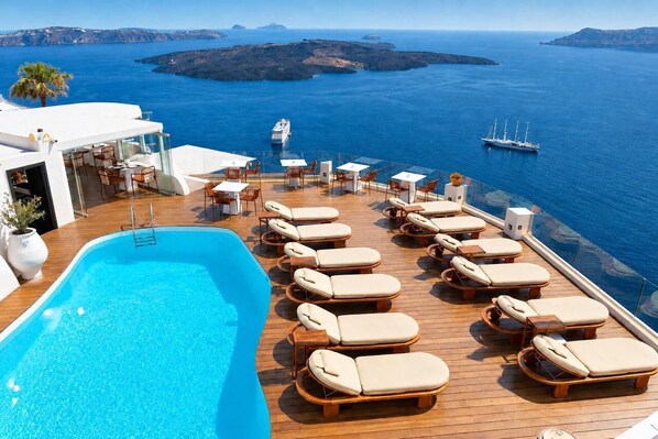 Un espace aménagé au bord de la piscine, avec des chaises longues et une piscine, offrant une vue sur la mer et les navires qui la sillonnent au loin.