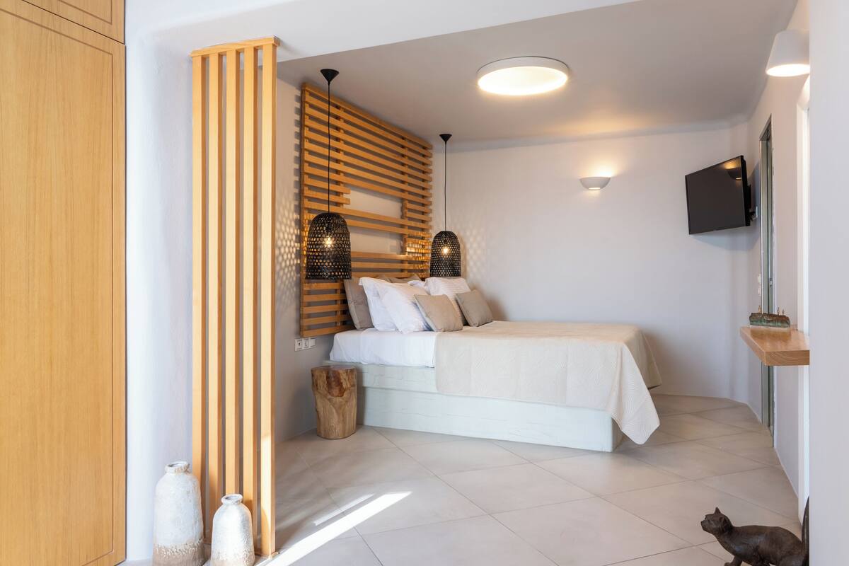 Une chambre à coucher avec un lit, des lattes en bois, une télévision et un chat.