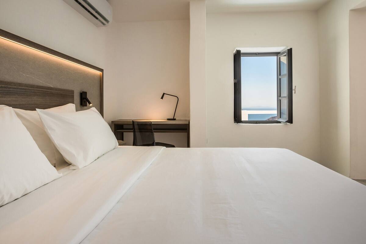 Une chambre d’hôtel avec un grand lit, un bureau avec une chaise, une fenêtre donnant sur un paysage agréable et un climatiseur fixé au mur.