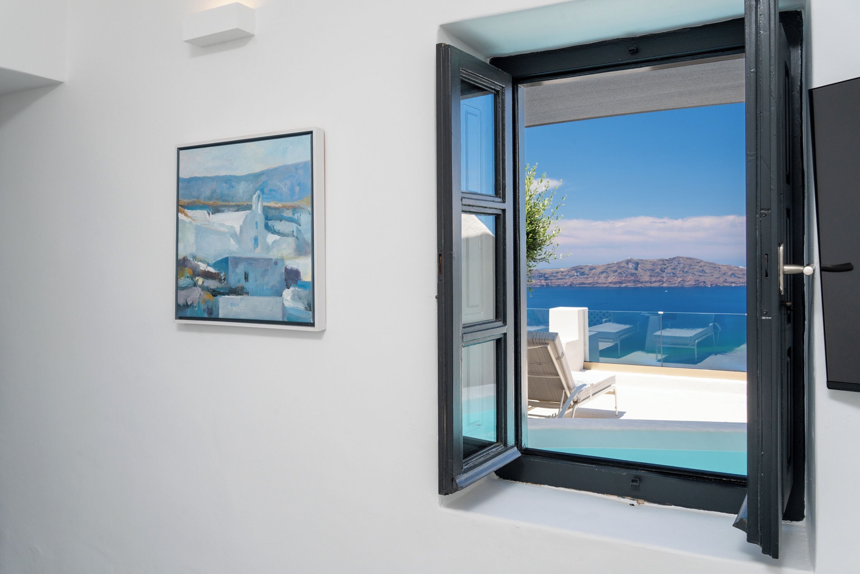 An open door to a balcony with a clear view of the sea and a mountain in the distance.