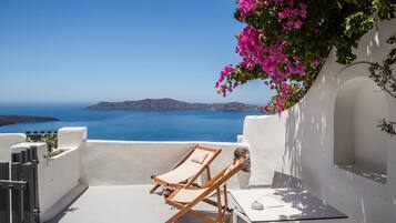 Eine Terrasse mit zwei Holzliegen und einem Tisch, mit Blick auf ein klares, blaues Meer und entfernte Inseln.