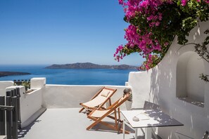 Une terrasse avec deux fauteuils de jardin en bois et une table, d’où l’on peut admirer une mer d’un bleu limpide et des îles lointaines.