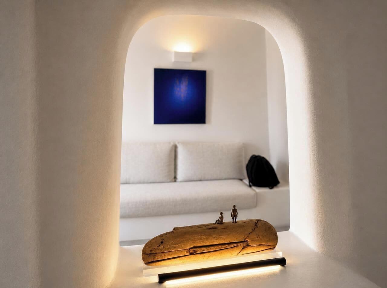Une pièce au décor minimaliste, avec un canapé blanc, un petit modèle de bateau en bois et un luminaire fixé au mur.