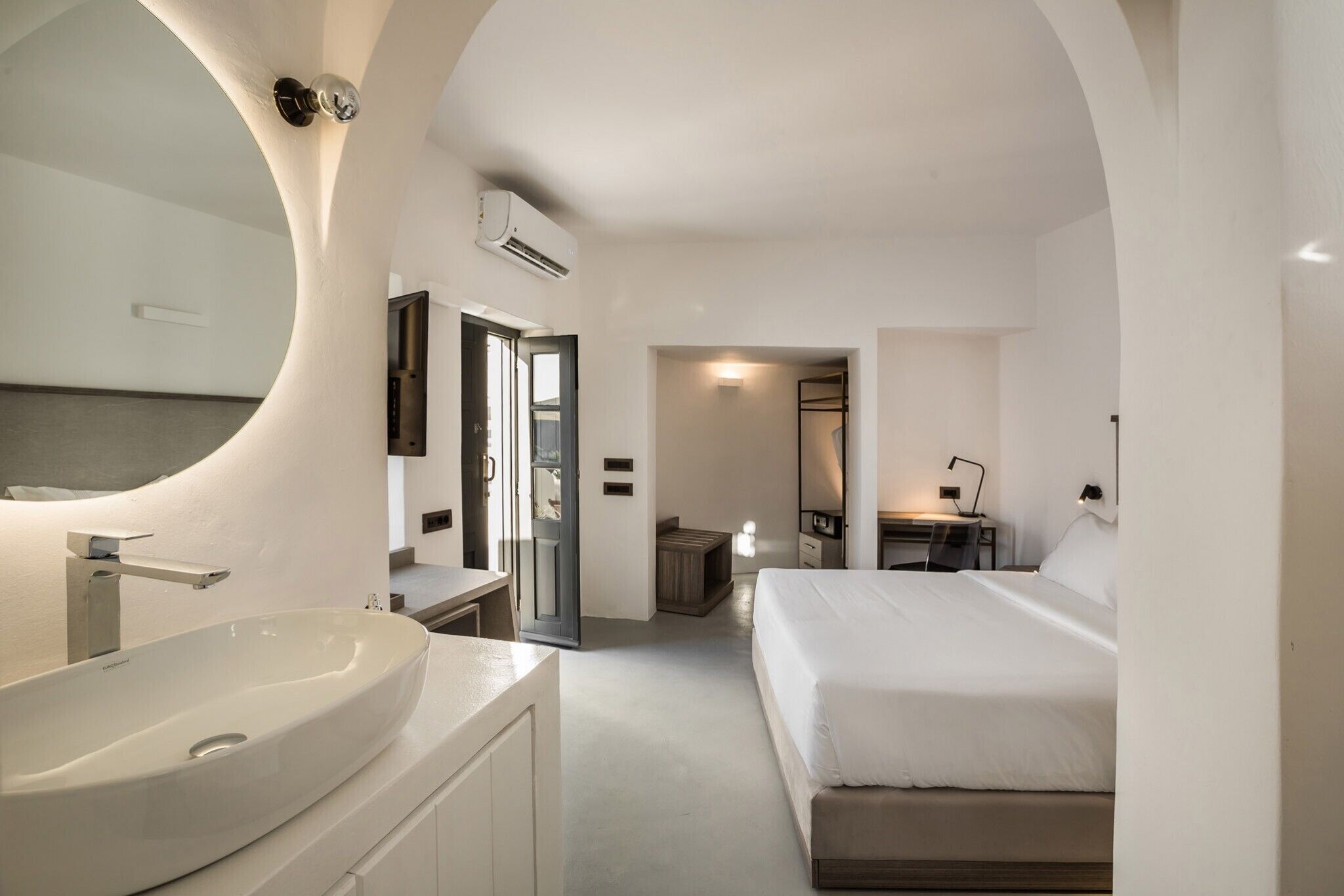 Una habitación de hotel moderna con un lavamanos ovalado grande, una cama, un escritorio y un espejo.