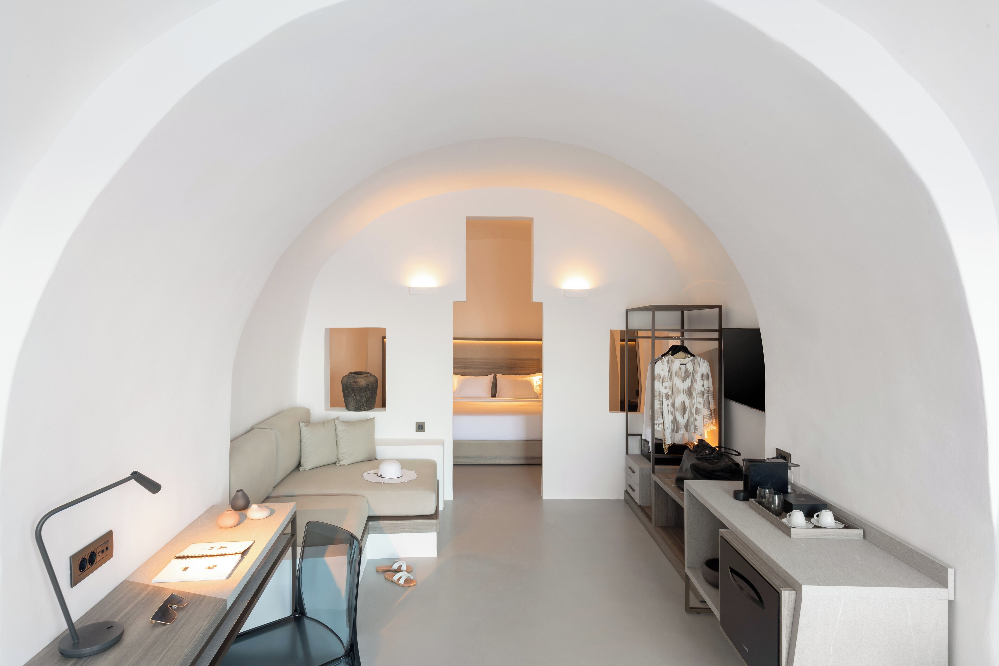 A compact hotel room with a desk, a bed, a sofa, and a vanity area.