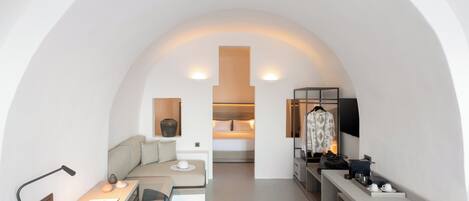 A compact hotel room with a desk, a bed, a sofa, and a vanity area.