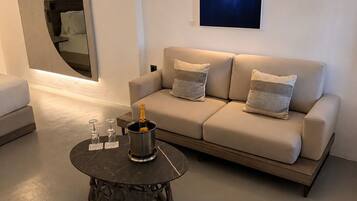 A modern living room with a sofa, a round coffee table with a bottle, and a wall-mounted TV.