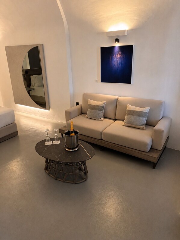 Un salon moderne avec un canapé, une table basse ronde sur laquelle se trouve une bouteille, et un téléviseur fixé au mur.