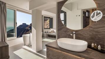 Une salle de bain moderne avec un grand lavabo ovale, un miroir rond et une vue sur les montagnes par une grande fenêtre.