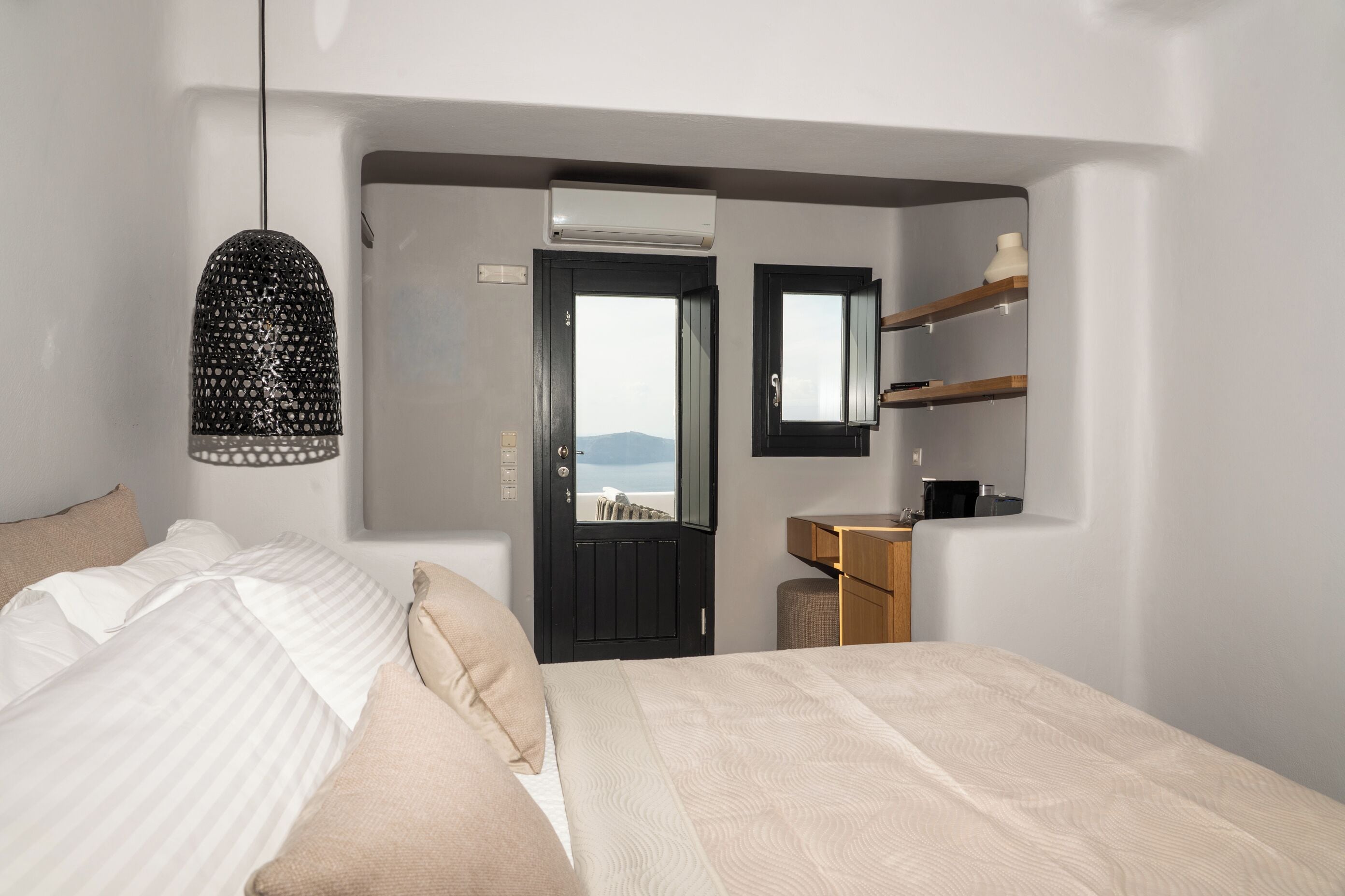 Une chambre à coucher comprenant un lit, un luminaire suspendu, une porte donnant sur un balcon et un petit bureau en bois avec un miroir.